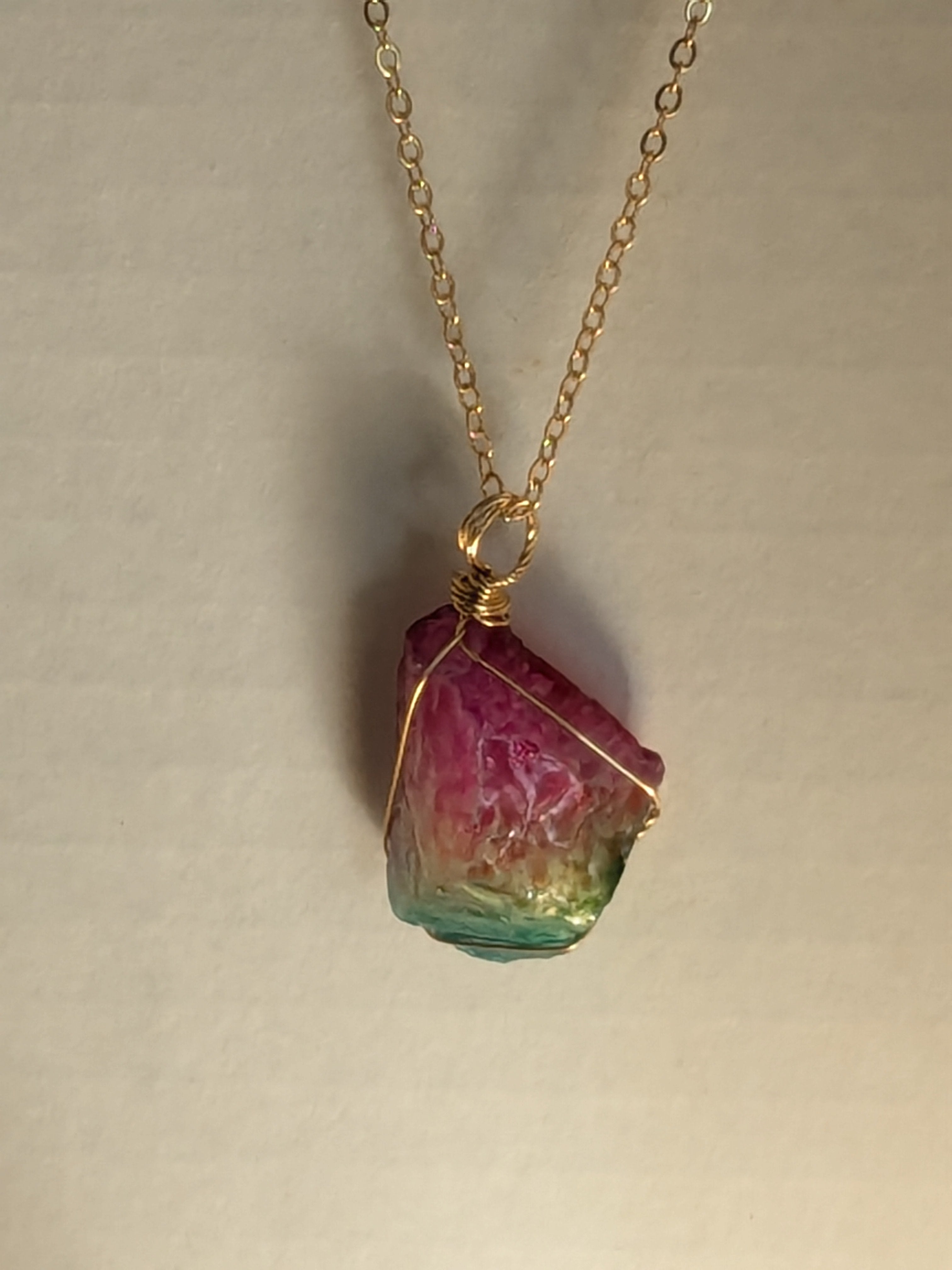 Gold chain necklace with multicolored crystal pendant: pink on top, green on bottom, wrapped in gold wire.