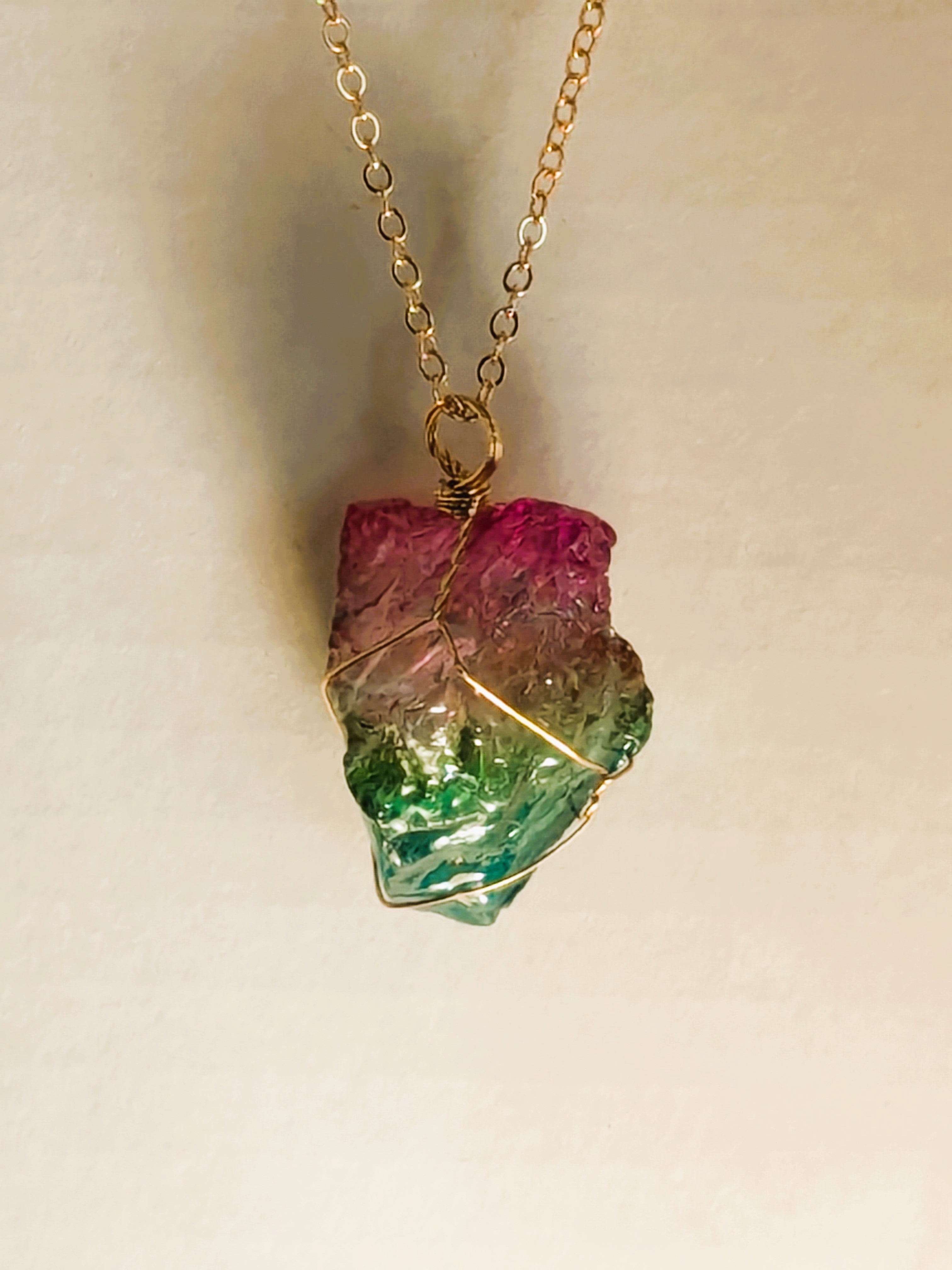 Gold chain necklace with multicolored crystal pendant: pink on top, green on bottom, wrapped in gold wire.