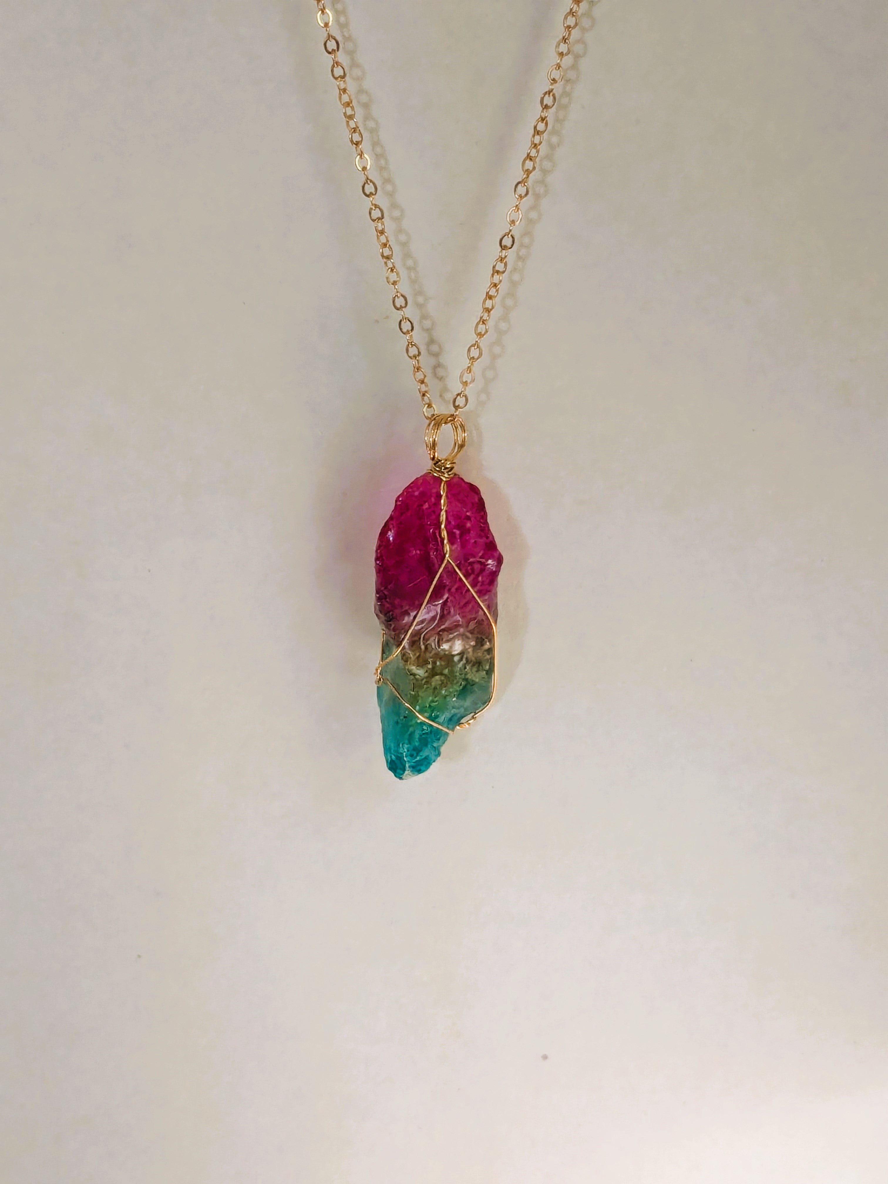 Gold chain necklace with multicolored crystal pendant: pink on top, green on bottom, wrapped in gold wire.